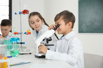 Schoolboy looking through microscope and his classmates at chemistry lesson