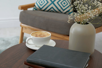 Cup of coffee and vase with flowers on wooden table in modern living room interior