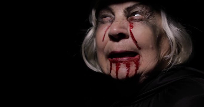 Old witch Halloween makeup. Elderly woman portrait with blood on her face.