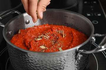 Woman cooking delicious tomato sauce in pan on stove, closeup