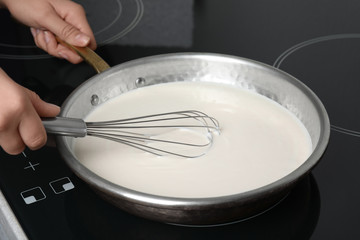 Woman cooking delicious creamy sauce in pan on stove, closeup