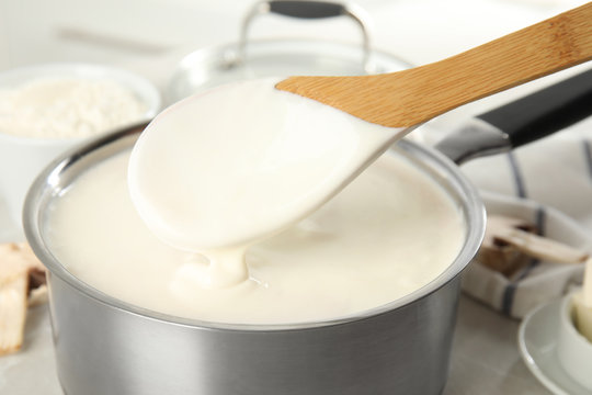 Spoon and pan with delicious creamy sauce, closeup view
