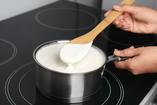 Woman cooking delicious creamy sauce in pan on stove, closeup