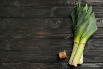 Fresh raw leeks on black wooden table, flat lay with space for text. Ripe onion
