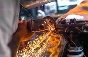 Worker cutting, grinding and polishing motorcycle metal part with sparks indoor workshop, close-up