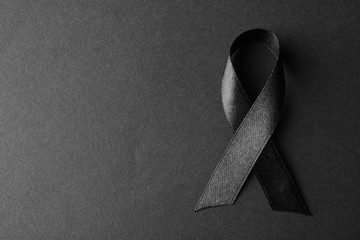 Black ribbon on dark background, top view with space for text. Funeral symbol