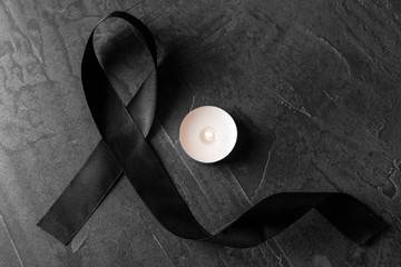 Black ribbon and burning candle on dark grey stone surface, top view. Funeral symbols