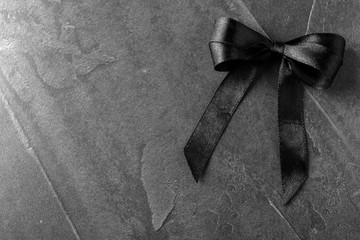 Black ribbon bow on dark grey stone surface, top view with space for text. Funeral symbol - obrazy, fototapety, plakaty