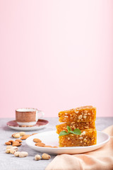 Traditional turkish candy cezerye made from caramelised melon, roasted walnuts, hazelnuts, cashew, pistachios on white ceramic plate and a cup of coffee on a gray and pink background. side view