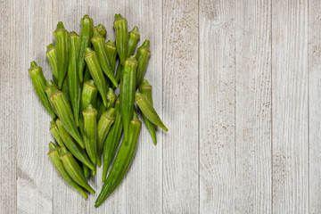 Fresh organic green okra in a heart shaped bowl isolated on a white wood board. with copy space.