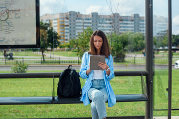 Happy woman uses a tablet or ebook on a tram station while waiting for public transport.