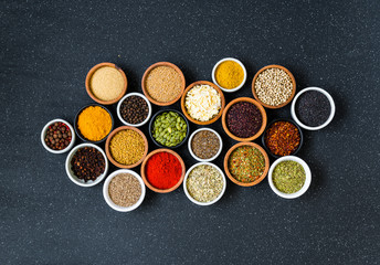 Variety of colorful spices, herbs, and seeds on black stone background