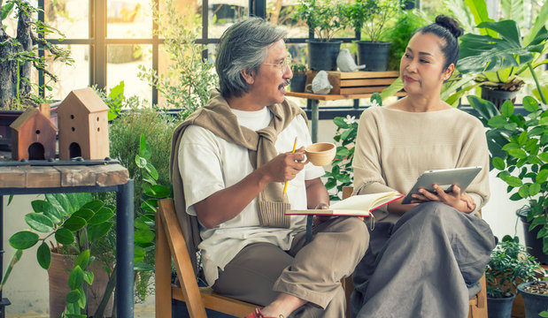 Asian elderly couple sitting and drinking tea and talking about plant in the Green House Relax time and lifestyle concept