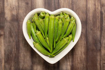 Fresh organic green okra in a heart shaped bowl isolated on a red wood board