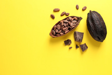 Cocoa pods with beans and chocolate pieces on yellow background, flat lay. Space for text