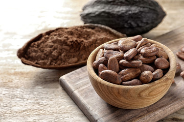 Bowl with cocoa beans on wooden table, space for text