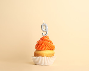 Birthday cupcake with number nine candle on beige background
