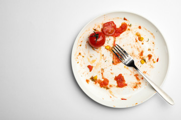 Dirty plate with food leftovers, tomato and fork on white background, top view