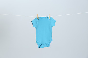 Cute baby onesie hanging on clothes line against light grey background. Laundry day