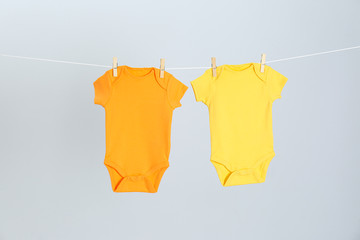 Different baby onesies hanging on clothes line against light grey background. Laundry day