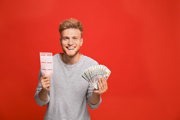 Portrait of happy young man with money fan and lottery ticket on red background
