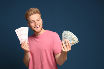 Portrait of happy young man with money and lottery tickets on blue background