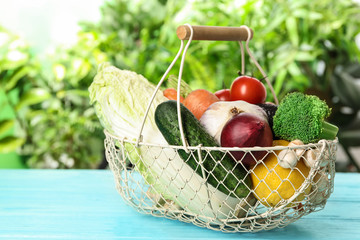 Fresh vegetables in metal basket on light blue wooden table against blurred green background