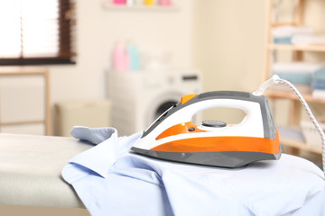 Modern electric iron and clean shirt on board in laundry room