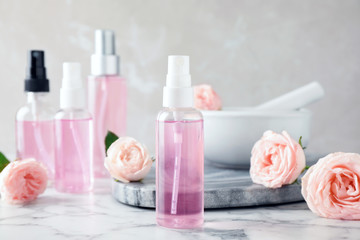 Bottles with rose essential oil and flowers on marble table
