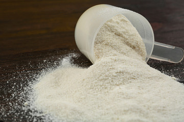 Overturned measuring scoop with protein powder on wooden table, closeup