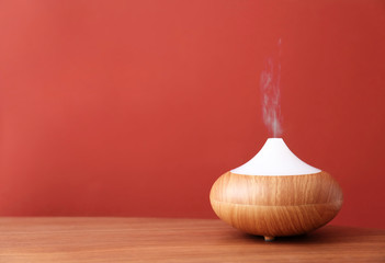 Essential oils diffuser on wooden table near red wall. Space for text