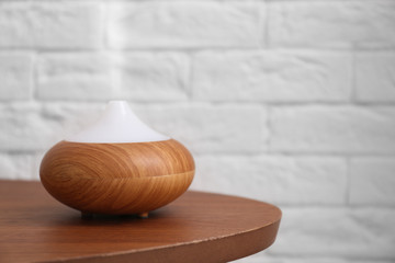 Essential oils diffuser on wooden table   against brick wall. Space for text