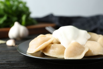 Delicious cooked dumplings with sour cream on dark wooden table, closeup