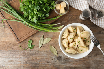 Delicious cooked dumplings with herbs on wooden table, flat lay