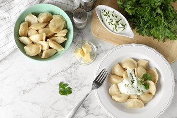 Delicious cooked dumplings with sour cream on white marble table, flat lay
