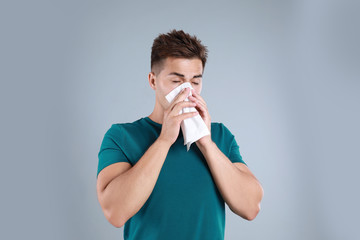 Young man suffering from allergy on grey background