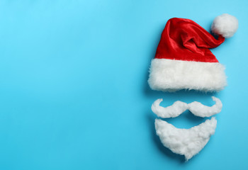 Santa Claus hat and beard on light blue background, flat lay. Space for text