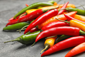 Different ripe chili peppers on grey table, closeup