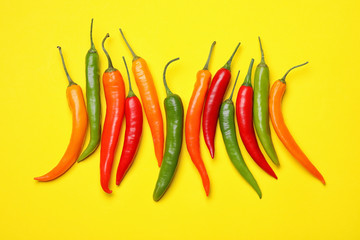 Different hot chili peppers on yellow background, flat lay