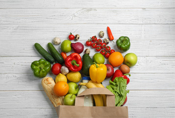 Paper bag with different groceries on white wooden table, flat lay