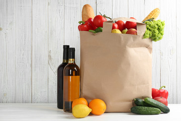 Shopping paper bag with different groceries on table against white wooden background. Space for text