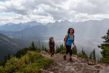 Adventurous Girl is hiking up a rocky mountain during a cloudy and rainy day. Taken from Mt Lady MacDonald, Canmore, Alberta, Canada.