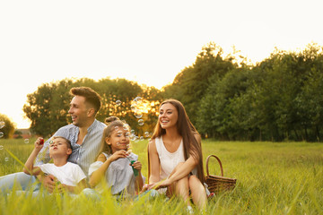 Happy family blowing soap bubbles in park at sunset. Summer picnic