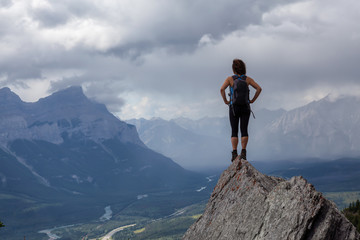 Adventurous Caucasian Girl is hiking up a rocky mountain during a cloudy and rainy day. Taken from Mt Lady MacDonald, Canmore, Alberta, Canada.