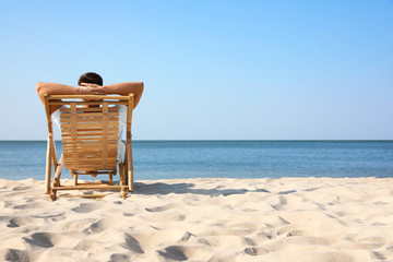 Young man relaxing in deck chair on sandy beach