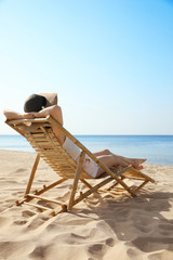 Young woman relaxing in deck chair on sandy beach