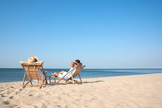 Young Couple Relaxing In Deck Chairs On Beach