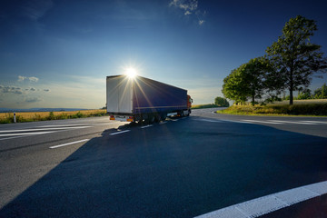 Truck driving on asphalt road under the glowing sun in the rural landscape