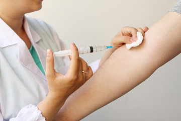 female doctor, nurse in white uniform makes an injection with a syringe in a man’s hand, medical concept, close-up, copy space