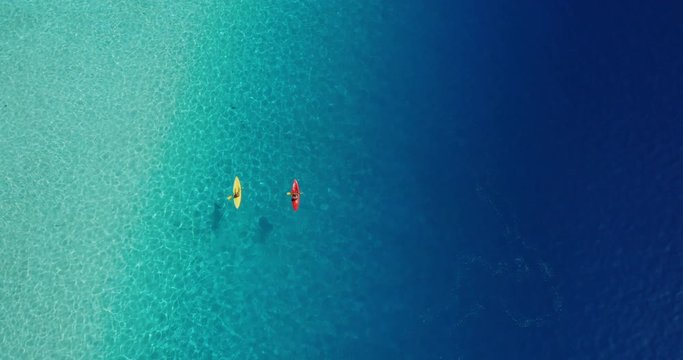 Wide aerial view of two kayakers paddling in a lagoon with pristine blue ocean water on a sunny sparkling day, amazing kayak adventures, kayaking through gorgeous water textures
